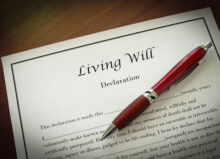 A document titled "Living Will" is laying on a table. On top of the document is a red pen.