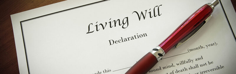 A document titled "Living Will" is laying on a table. On top of the document is a red pen.