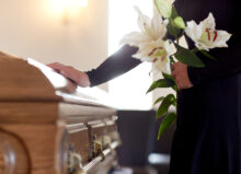 A woman holds flowers and places her hand on a funeral casket