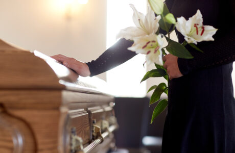 A woman holds flowers and places her hand on a funeral casket